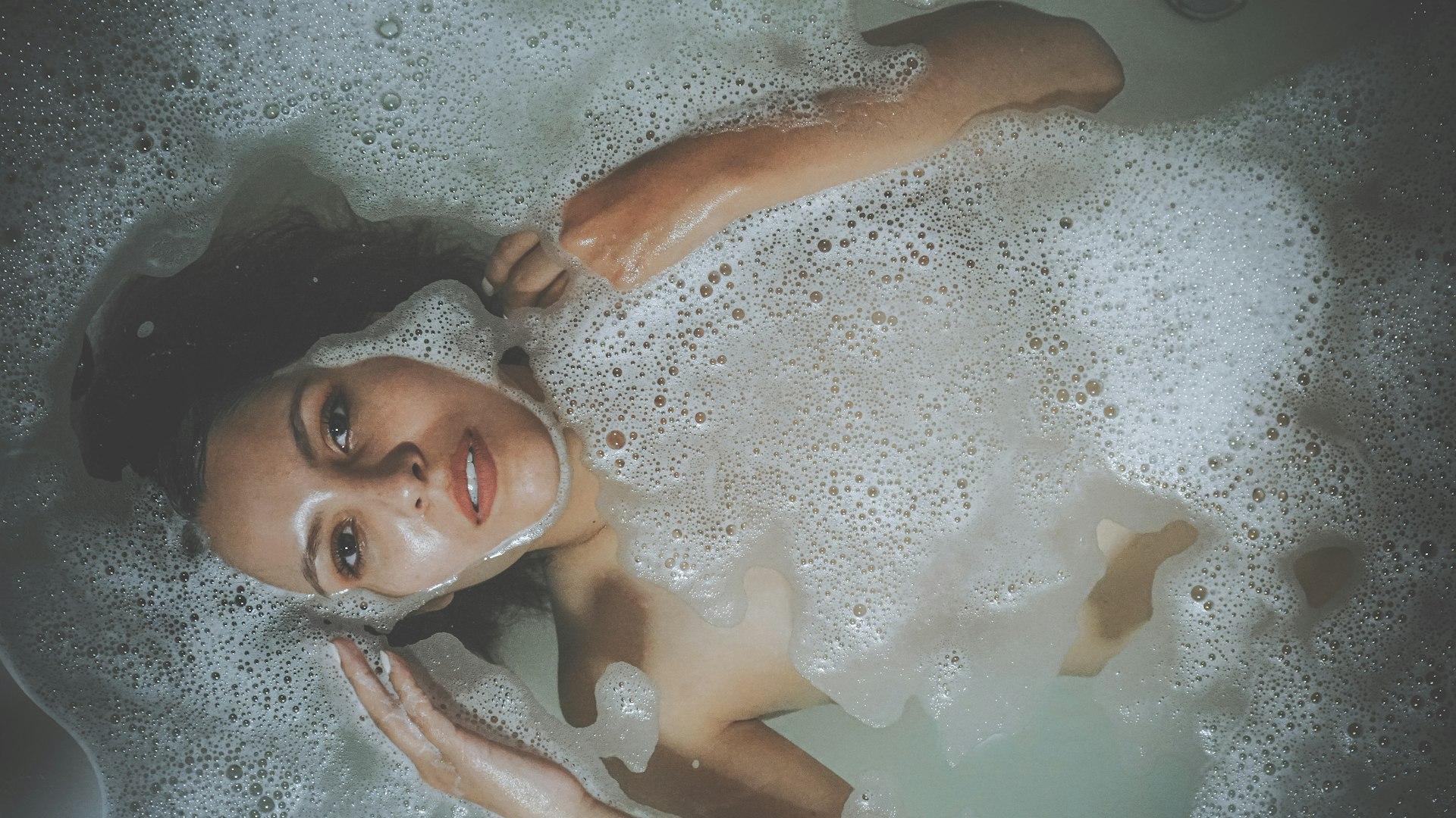 a woman laying in a bathtub with foam on her face